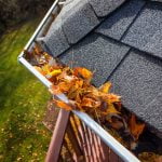 Roof gutters filled with autumn leaves, green lawn below, part of the patio is showing.