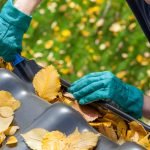 Man manually cleaning gutters from yellow leaves and debris; he's wearing blue gloves.