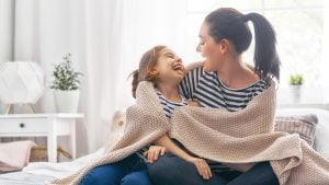 A girl and her mother enjoy sunny morning wrapped in blankets, laughing