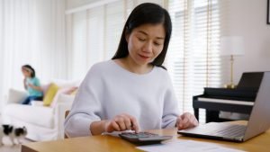 Asian mom happy, calculating on a calculator, child in the back playing with pet