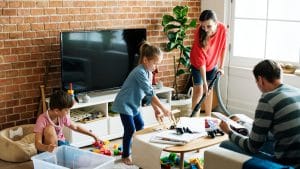 Family spending time together. Mum cleaning, children organising their toys, dad going through magazines.