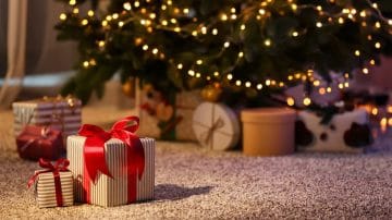 A Christmas tree with lights. A few presents on a carpeted floor protector