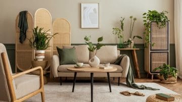 A living room with sofa, table with 2 cups, a few green plants and an armchair. Slippers on the floor and a white cosy carpet.