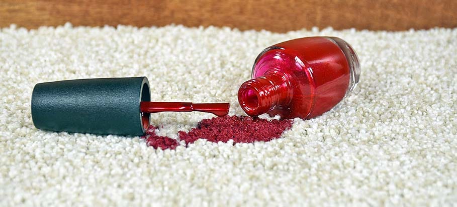 Opened bottle of red nail polish dropped on a white carpet.