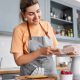 culinary, baking and cooking food concept - happy smiling young woman making layer cake and spreading topping cream on kitchen at home