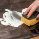 A hand cleaning an induction stove top with a yellow sponge.